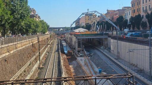 L’immagine mostra il cantiere della stazione Pigneto FS durante la realizzazione della nuova struttura. Sono visibili elementi in cemento armato e il solaio in costruzione sopra la circonvallazione Casilina. L’area appare delimitata dalle opere di cantiere e occupata dalle strutture provvisorie necessarie alla costruzione della nuova fermata ferroviaria.