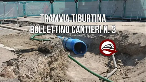 Fotogramma del cantiere della tramvia Tiburtina con un ampio scavo dove vengono posate le nuove tubazioni dell'Acqua Vergine. Sono presenti escavatori, mezzi di cantiere e personale impegnato nelle operazioni di installazione. L'immagine evidenzia la complessità dell'intervento sotterraneo, necessario per spostare i sottoservizi prima della costruzione dell'infrastruttura tranviaria lungo via Tiburtina.